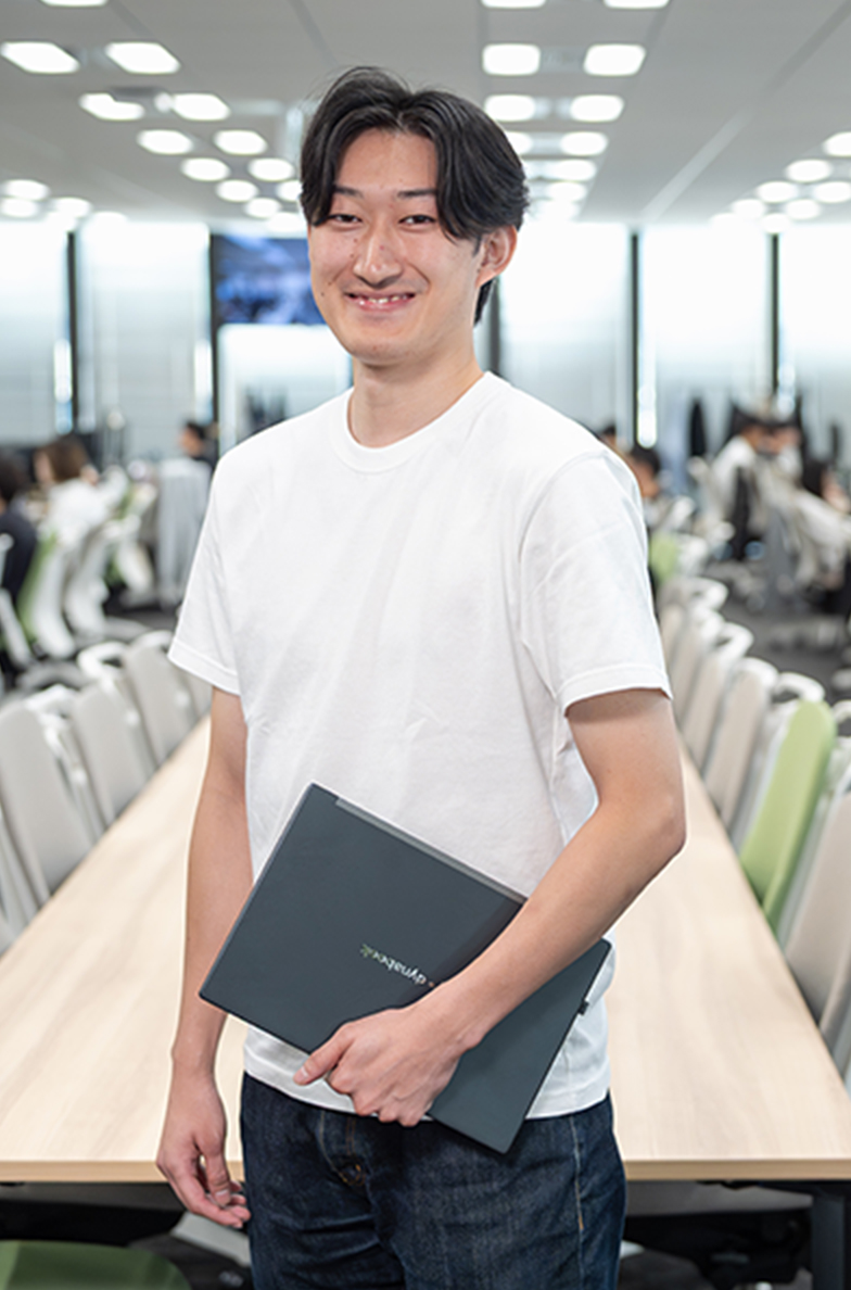 ノートパソコンを手に、笑顔で直立している写真