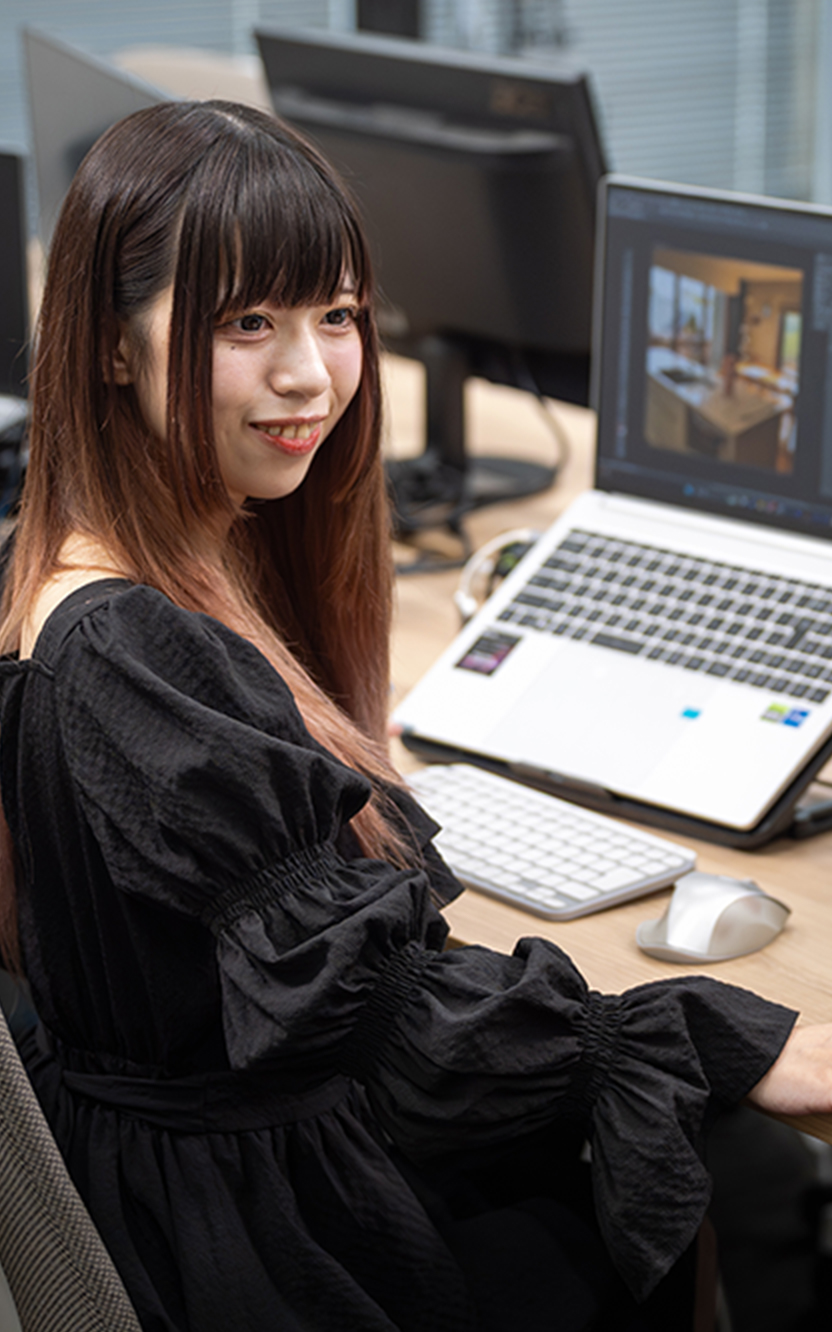 作業デスクに座った状態で体をこちらに向け他のスタッフと話をしている様子