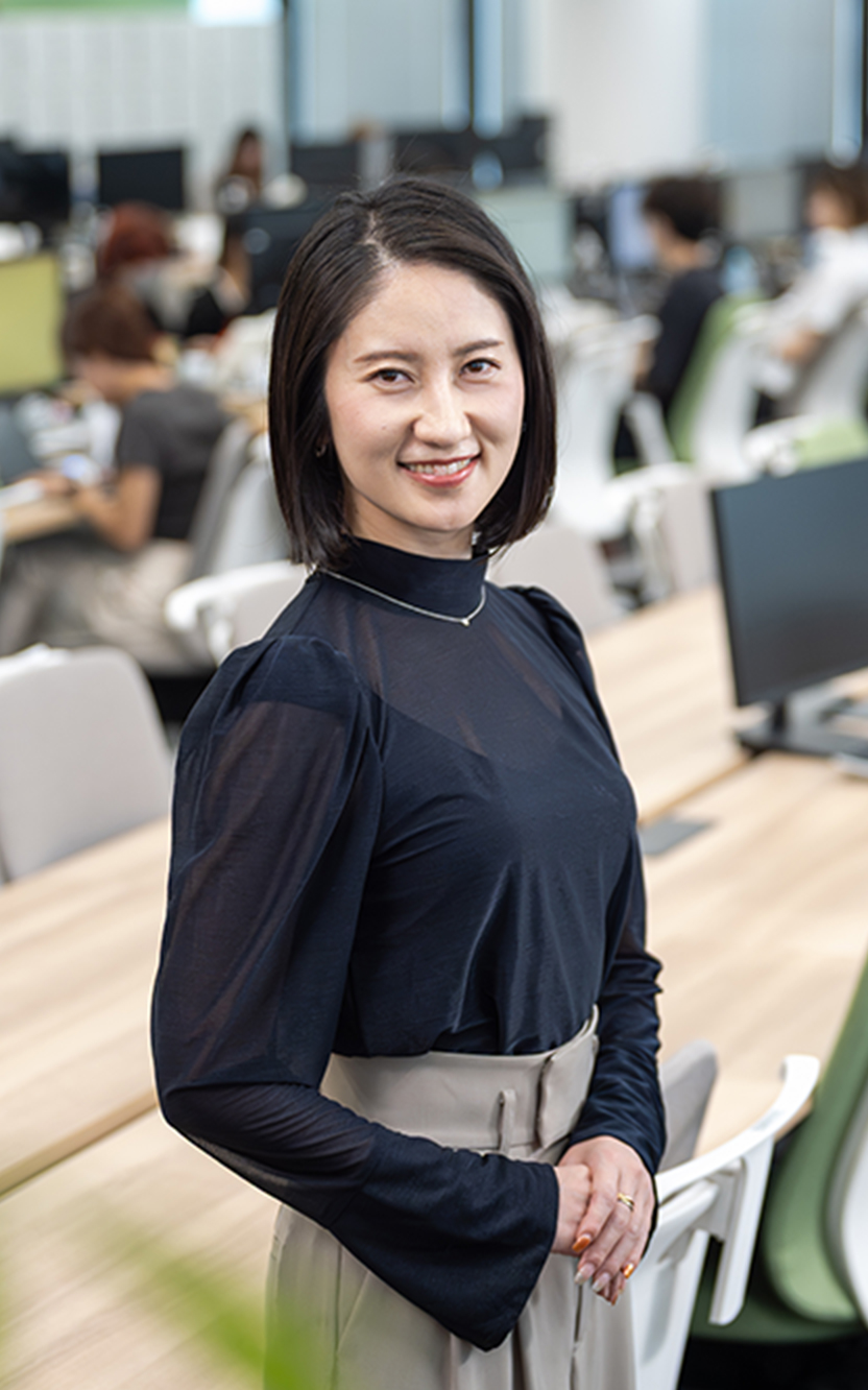 手を前に組み笑顔で立っている様子