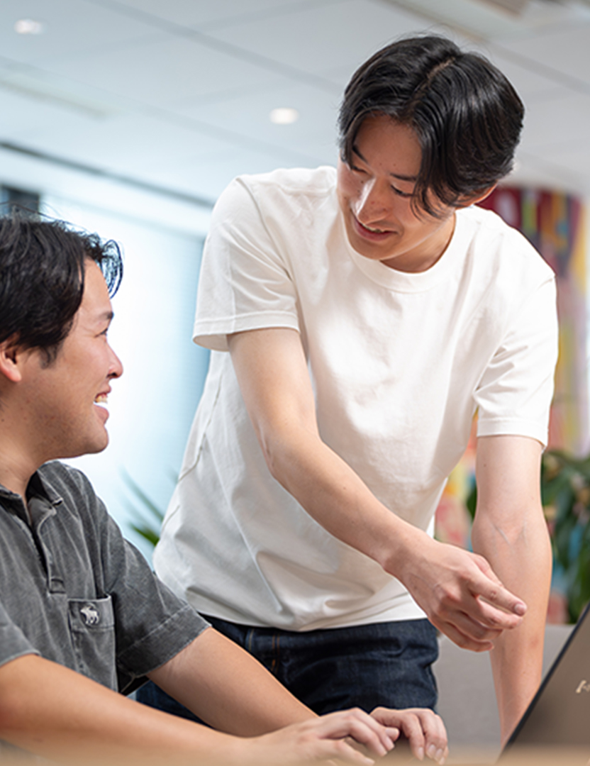 ノートパソコンを指さしながら他のスタッフと会話している様子